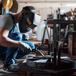 Portrait of a young worker at a large metalworking plant. The welder engineer works in a protective mask.
